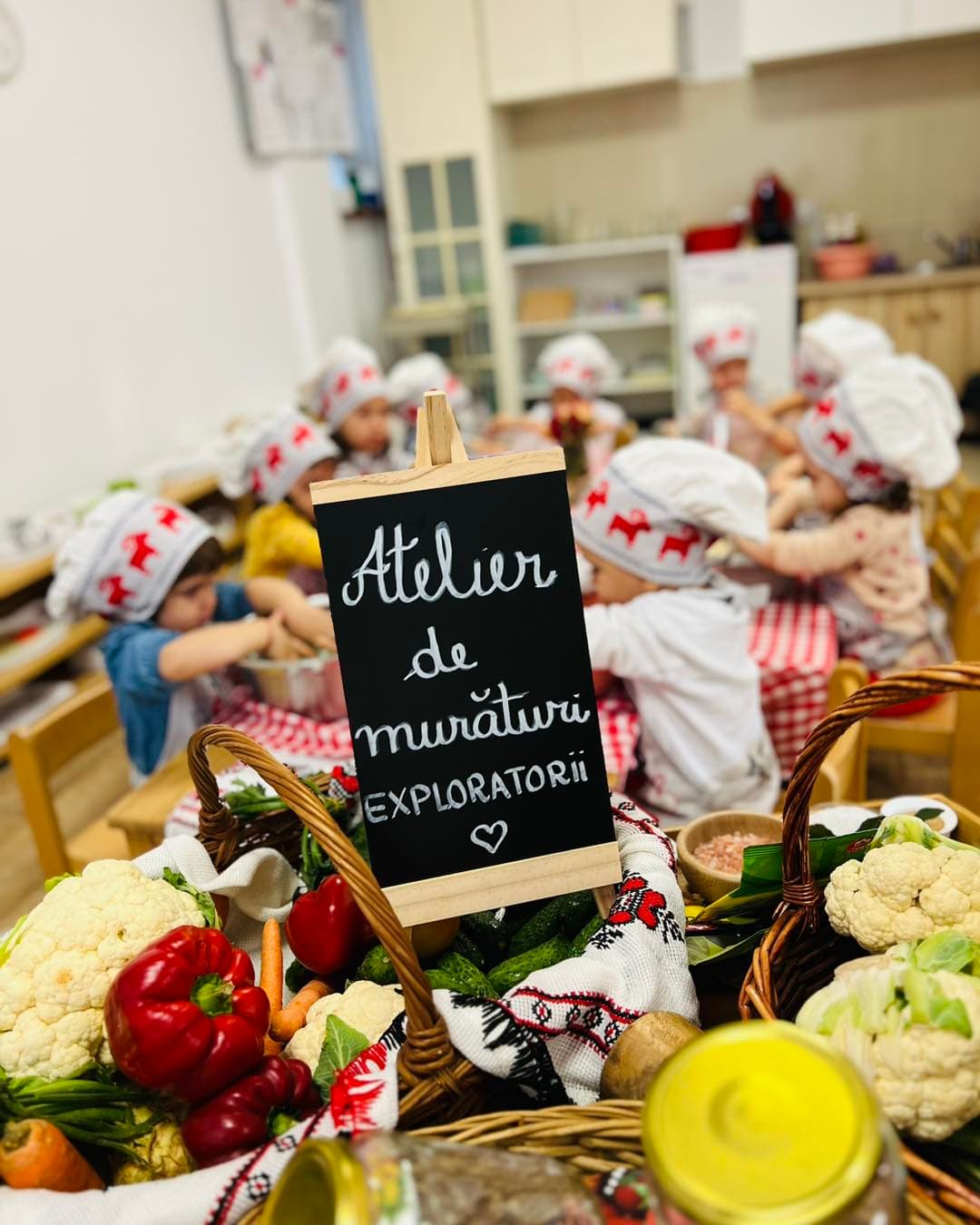 Tăbliță de scris cu inscripția „Atelier de murături”, cu un coș de legume în prim-plan